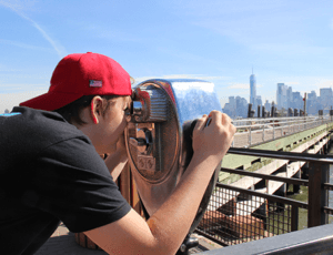 Middle school male looking at New York City skyline with a viewfinder on a sunny day