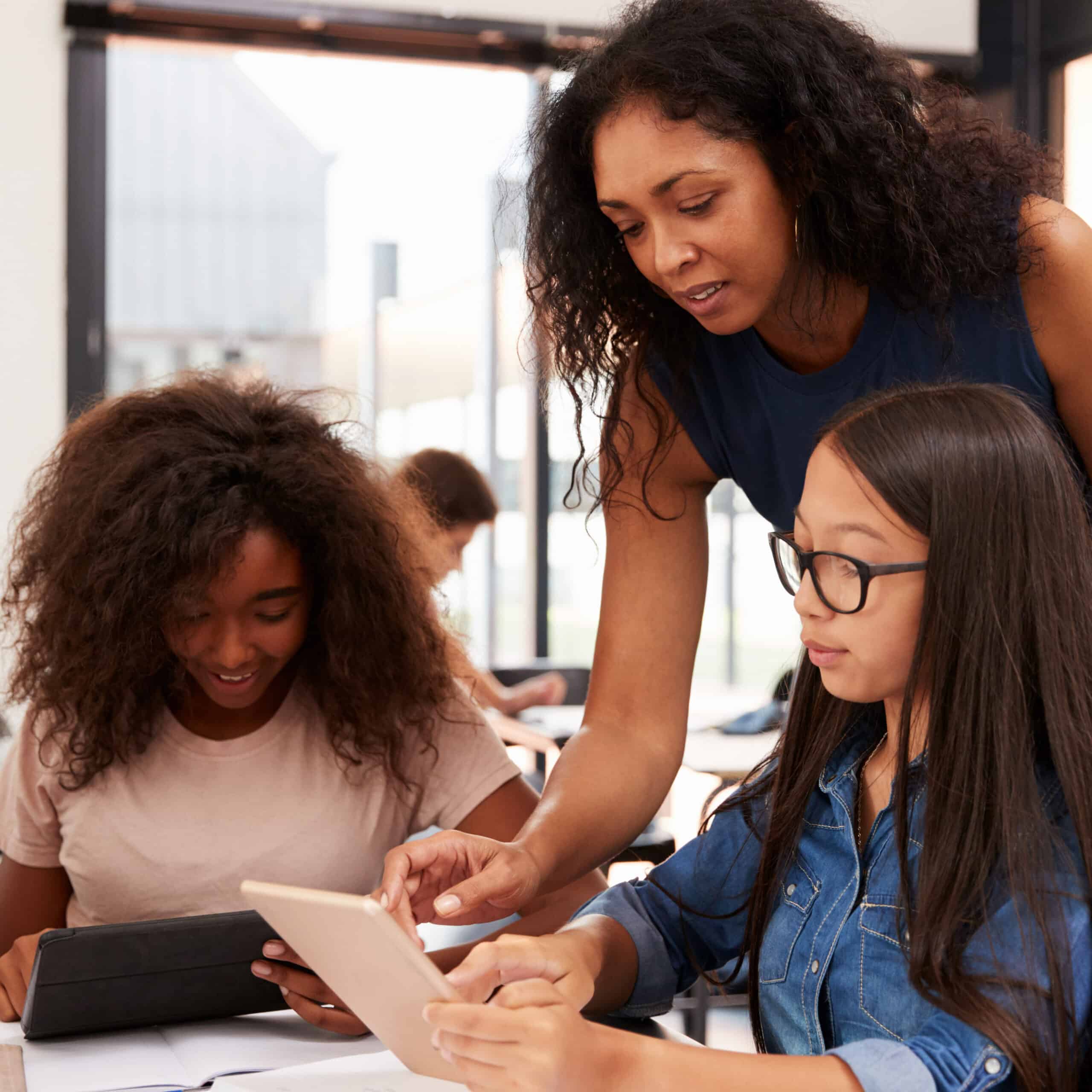 Female teacher helping female students as they work on ipad.